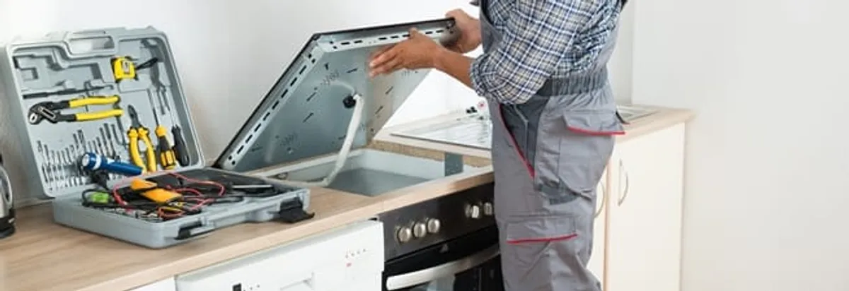 Cooktop repair technician lifting a built-in stovetop for service in South Bend, IN